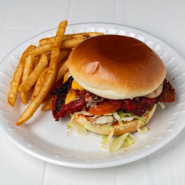 A chicken burger with cheese, lettuce, and tomato, served with a side of fries on a white plate.