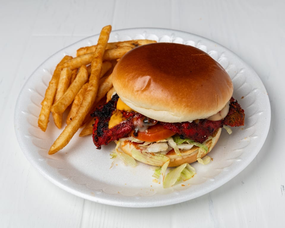 A chicken burger with cheese, lettuce, and tomato, served with a side of fries on a white plate.