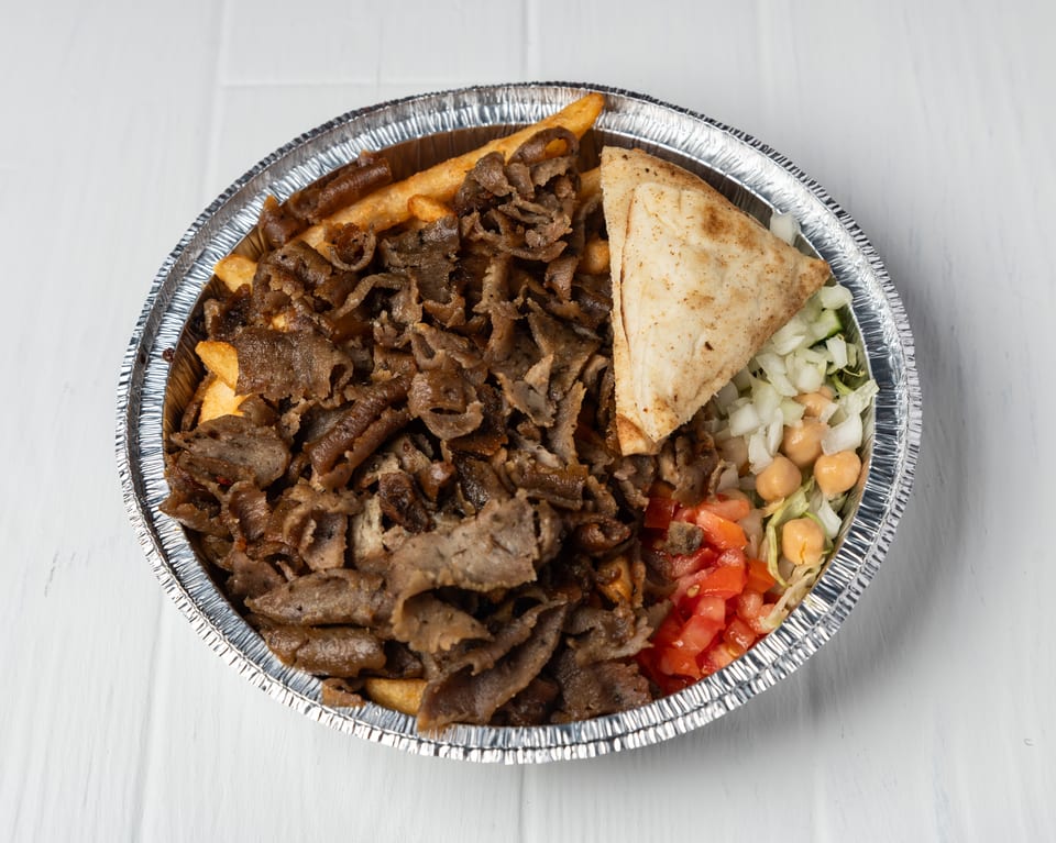 A gyro platter in a foil container with meat, fries, pita bread, and salad.