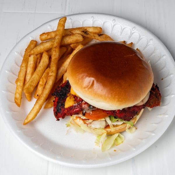 A chicken burger with cheese, lettuce, and tomato, served with a side of golden fries.