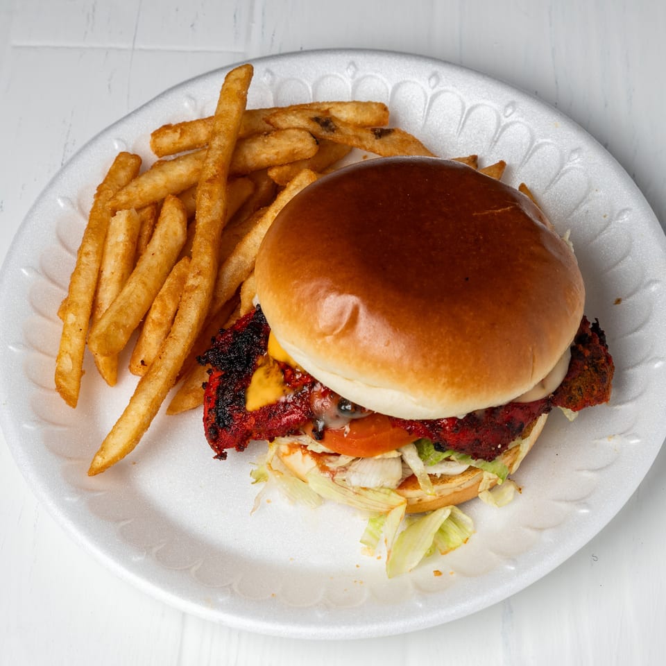 A chicken burger with cheese, lettuce, and tomato, served with a side of golden fries.
