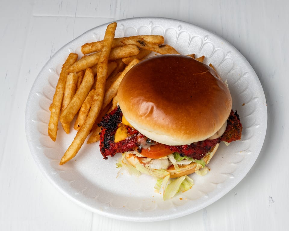A chicken burger with cheese, lettuce, and tomato, served with a side of golden fries.