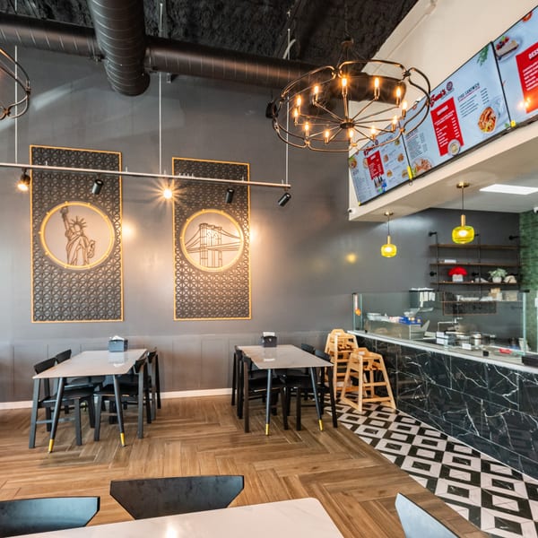 Modern restaurant interior with dark gray walls, wood-patterned floor, black tables, and digital menu boards.