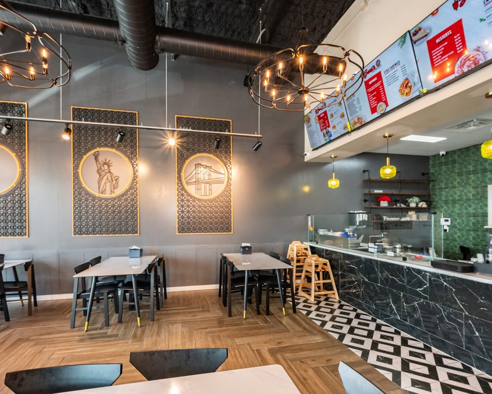 Modern restaurant interior with dark gray walls, wood-patterned floor, black tables, and digital menu boards.