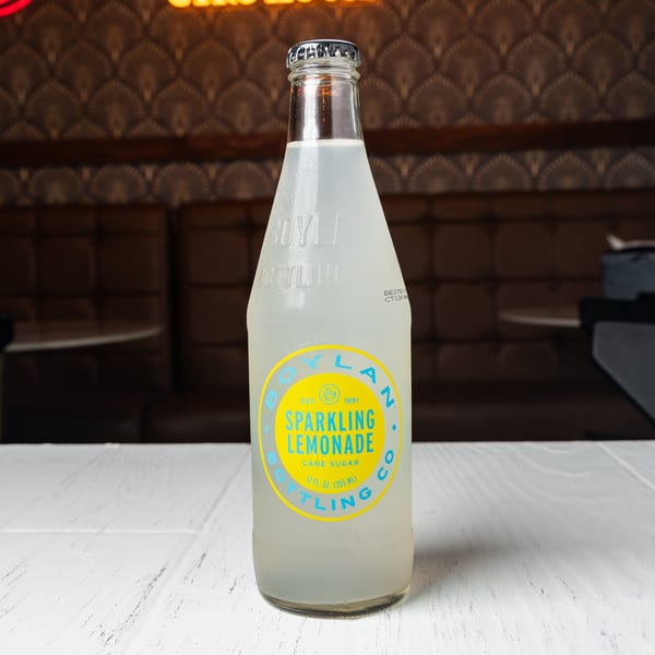 A bottle of Boylan Sparkling Lemonade on a white table with a patterned wall and booth in the background.