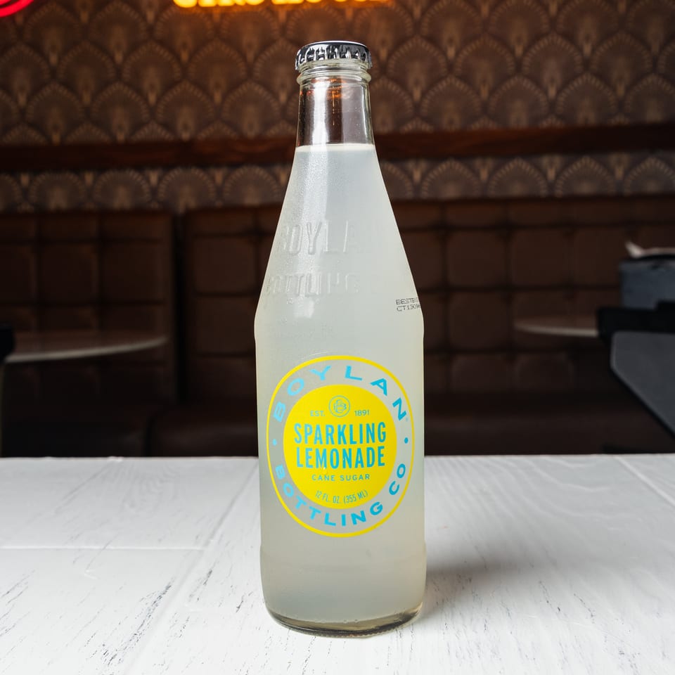 A bottle of Boylan Sparkling Lemonade on a white table with a patterned wall and booth in the background.