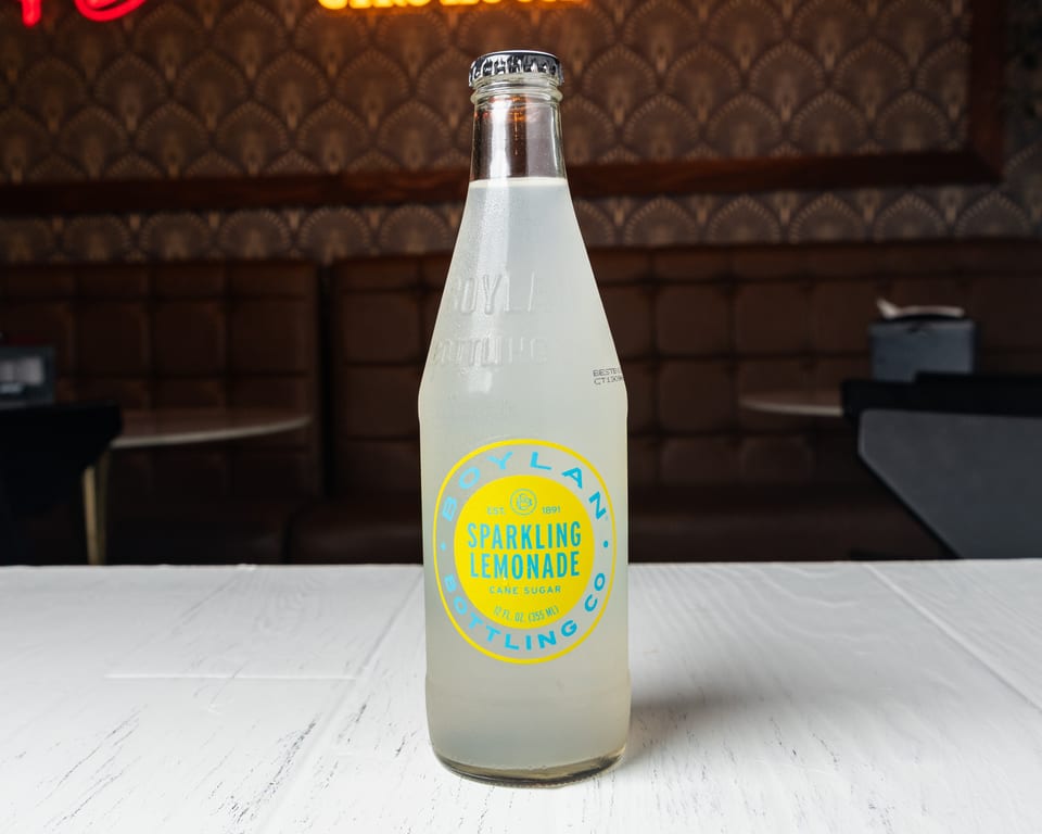 A bottle of Boylan Sparkling Lemonade on a white table with a patterned wall and booth in the background.