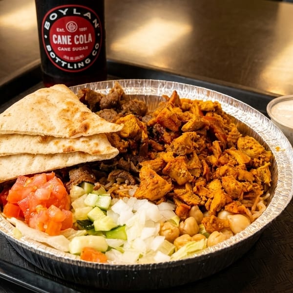A foil bowl with chicken, beef, pita, salad, and sauces, with a Boylan Cane Cola.