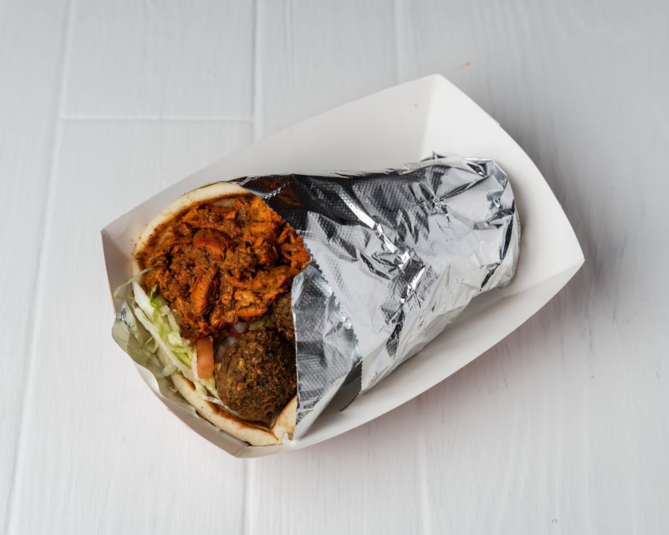 A chicken and falafel pita wrap, partially wrapped in foil, sits in a white paper tray.