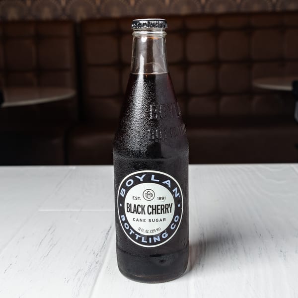 A cold Boylan Black Cherry soda bottle with condensation on a white table.