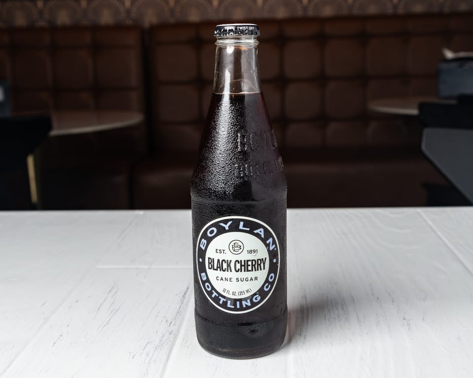 A cold Boylan Black Cherry soda bottle with condensation on a white table.