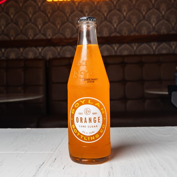 A Boylan Orange Cane Sugar soda bottle sits on a white table in a restaurant.