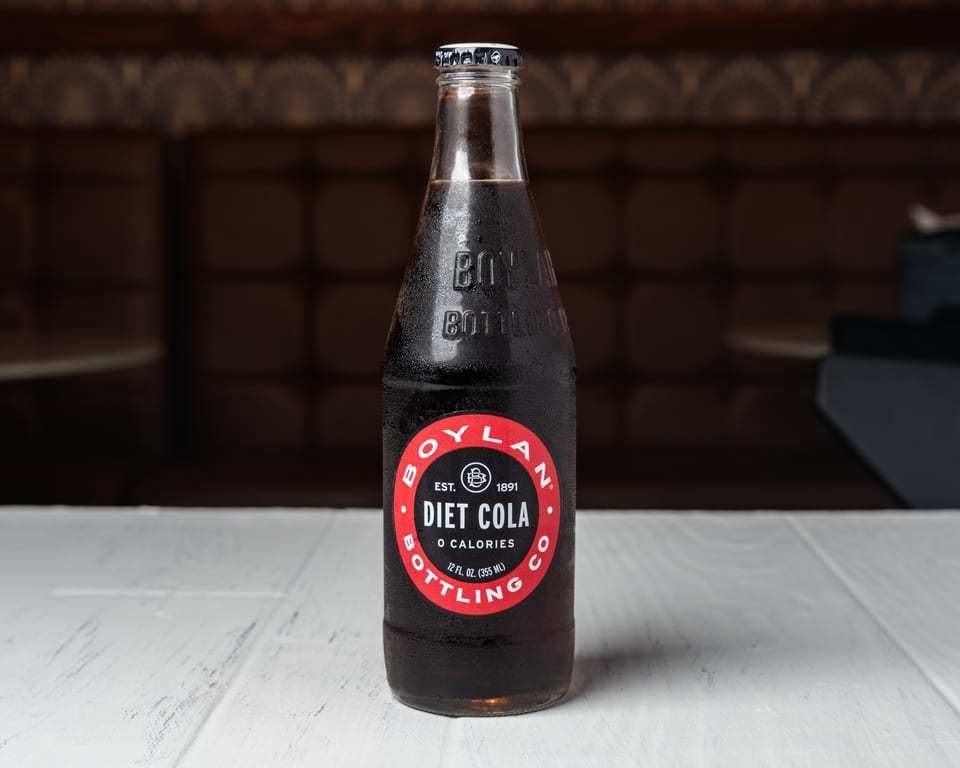 A cold, condensation-covered bottle of Boylan Diet Cola sits on a white table.