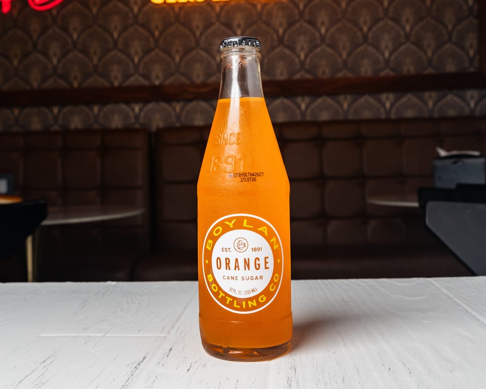 A Boylan Orange Cane Sugar soda bottle on a white table in a restaurant booth.
