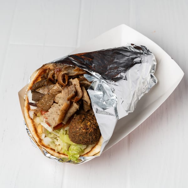 Gyro with meat, falafel, lettuce, and onions in a pita, partially wrapped in foil.