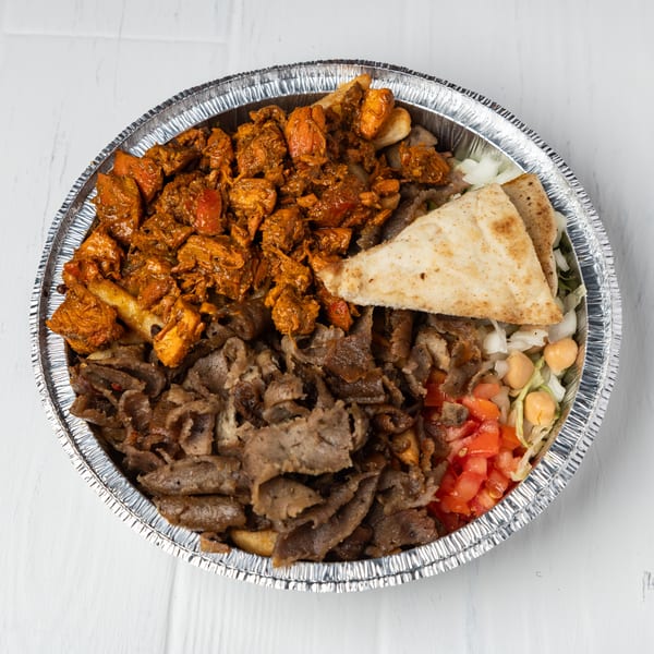A foil container filled with chicken, gyro meat, pita bread, lettuce, chickpeas, and diced tomatoes.