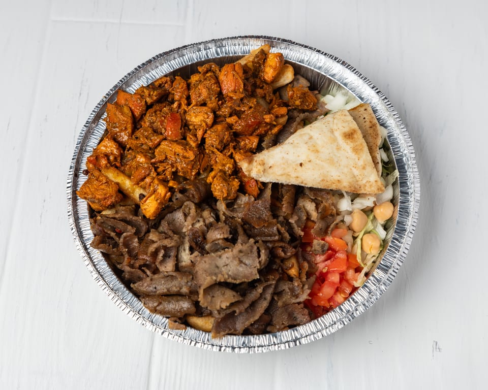 A foil container filled with chicken, gyro meat, pita bread, lettuce, chickpeas, and diced tomatoes.
