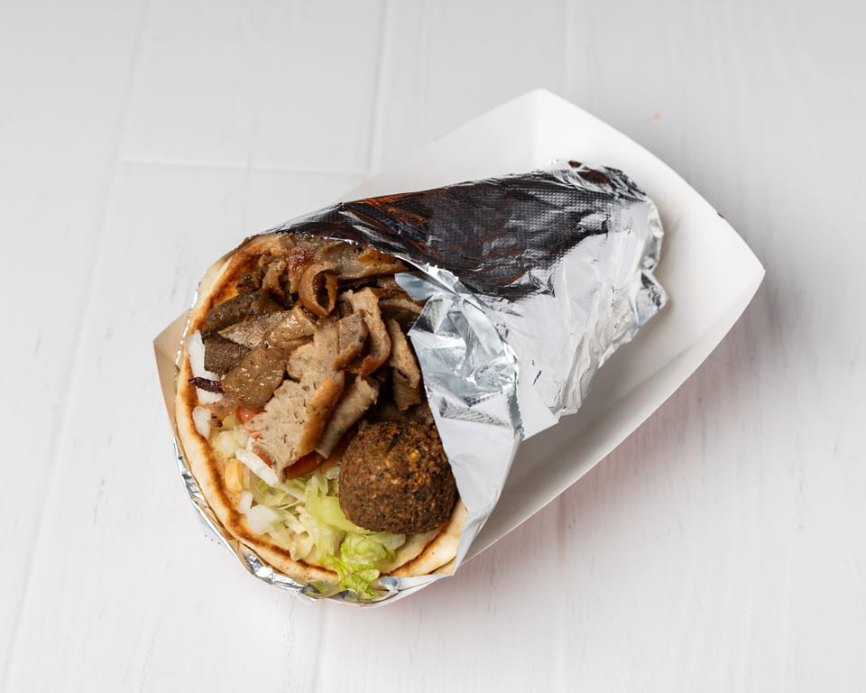 Gyro and falafel wrapped in pita bread with lettuce, tomatoes, and onions, in a white tray.