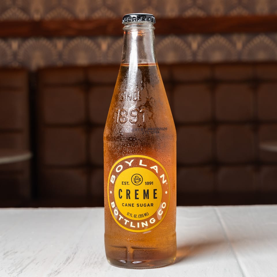 A condensation-covered bottle of Boylan Creme Cane Sugar soda sits on a white table.