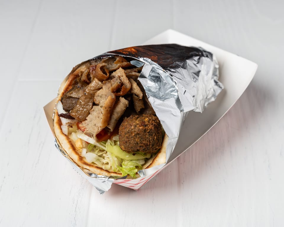 A gyro with meat, lettuce, onions, and a falafel ball, wrapped in foil in a paper tray.