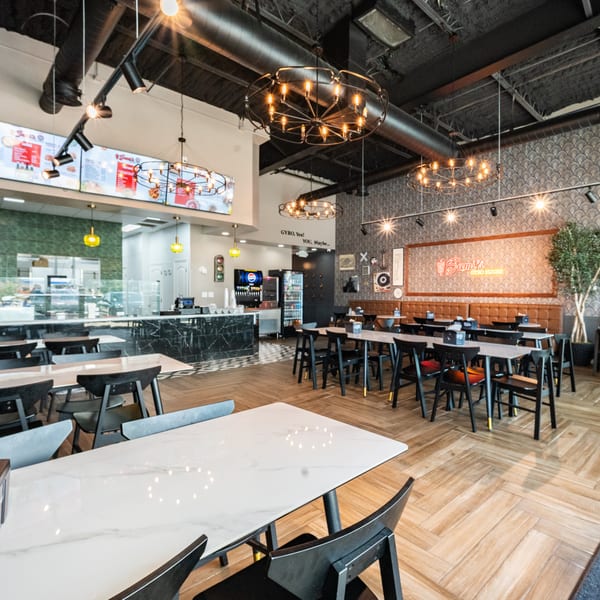 Modern restaurant interior with black and white tables, black chairs, and a counter with menu boards.