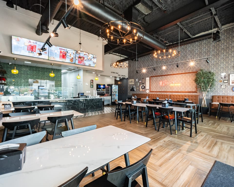 Modern restaurant interior with black and white tables, black chairs, and a counter with menu boards.