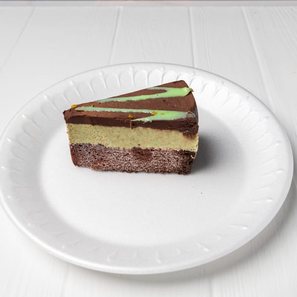 Slice of layered chocolate and pistachio cake with green drizzle on a white plate.