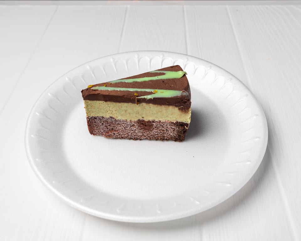 Slice of layered chocolate and pistachio cake with green drizzle on a white plate.