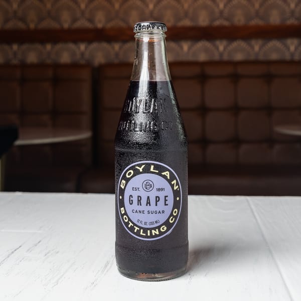 A Boylan Grape Cane Sugar soda bottle with condensation sits on a white table in a restaurant.