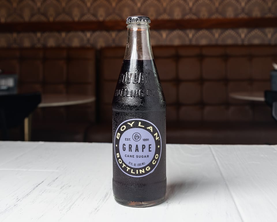 A Boylan Grape Cane Sugar soda bottle with condensation sits on a white table in a restaurant.