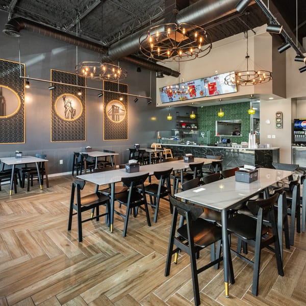 Modern restaurant interior with dark gray walls, light wood floors, black tables, and New York City themed decor.