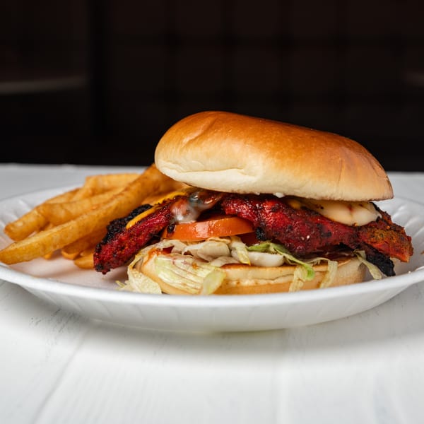 Spicy chicken sandwich with lettuce, tomato, cheese, and fries on a white plate.