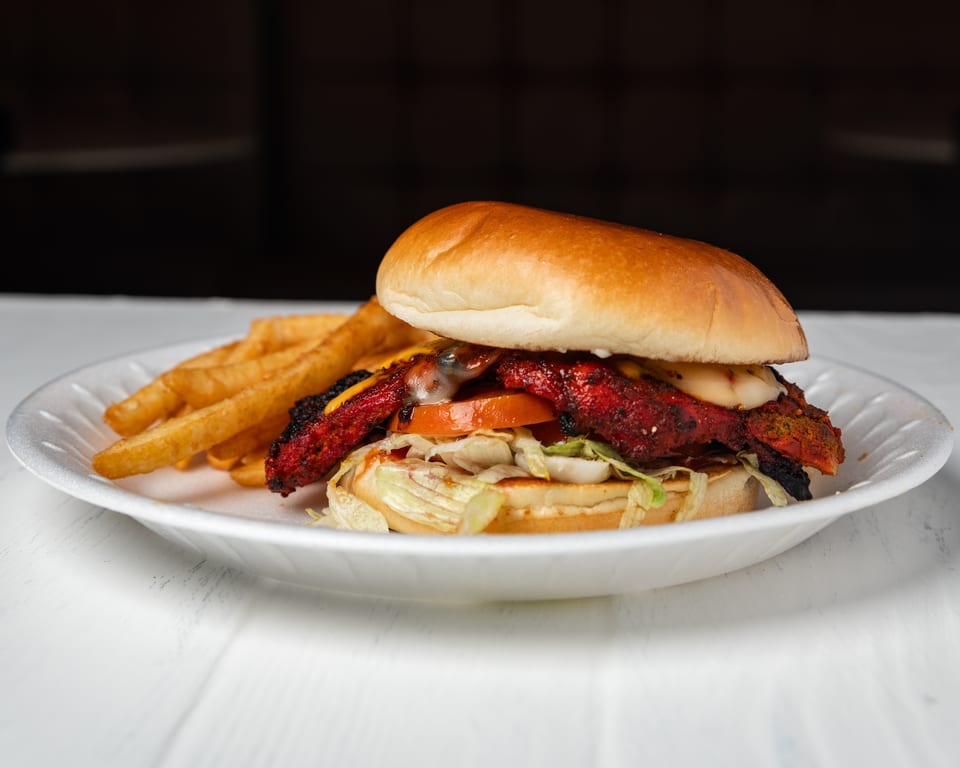 Spicy chicken sandwich with lettuce, tomato, cheese, and fries on a white plate.