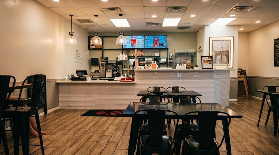 Interior of a modern fast-casual restaurant with tables, chairs, and a service counter with menu boards.