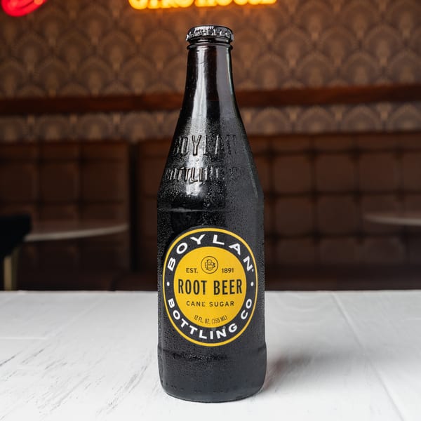 A cold bottle of Boylan Root Beer with a yellow label sits on a white table.