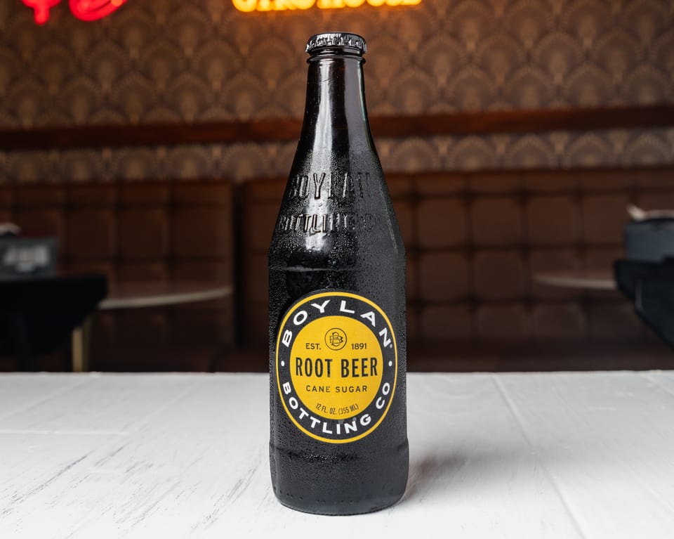 A cold bottle of Boylan Root Beer with a yellow label sits on a white table.
