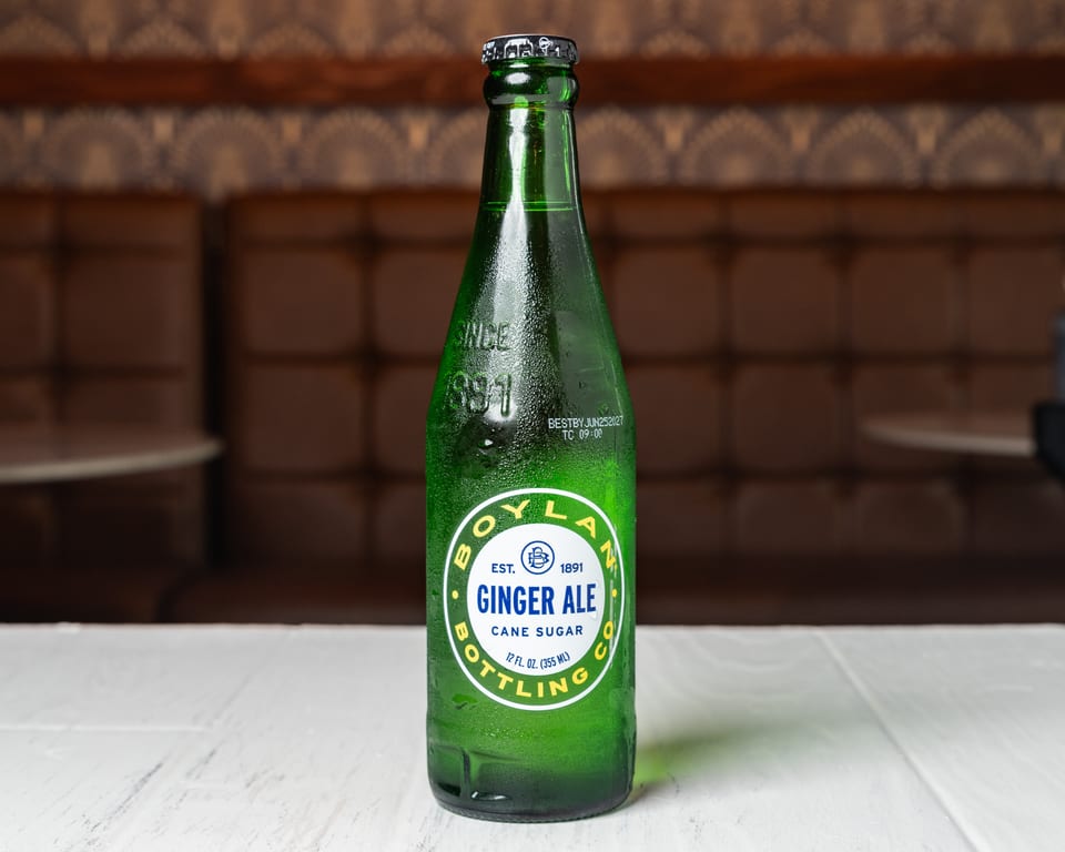 A cold, green glass bottle of Boylan Ginger Ale with a white label on a white table.