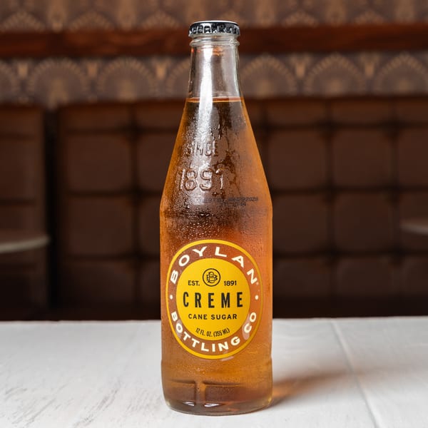 A condensation-covered bottle of Boylan Creme Cane Sugar soda sits on a white table.