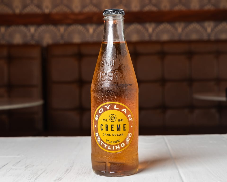 A condensation-covered bottle of Boylan Creme Cane Sugar soda sits on a white table.