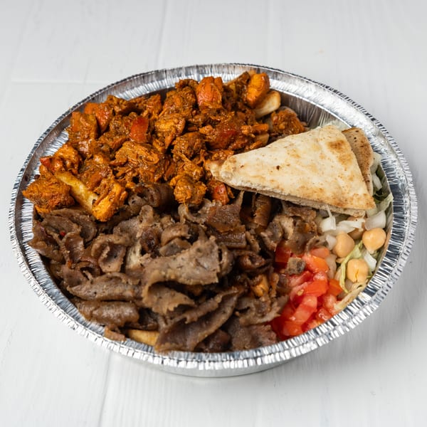 A foil container filled with chicken, gyro meat, pita bread, lettuce, chickpeas, and diced tomatoes.