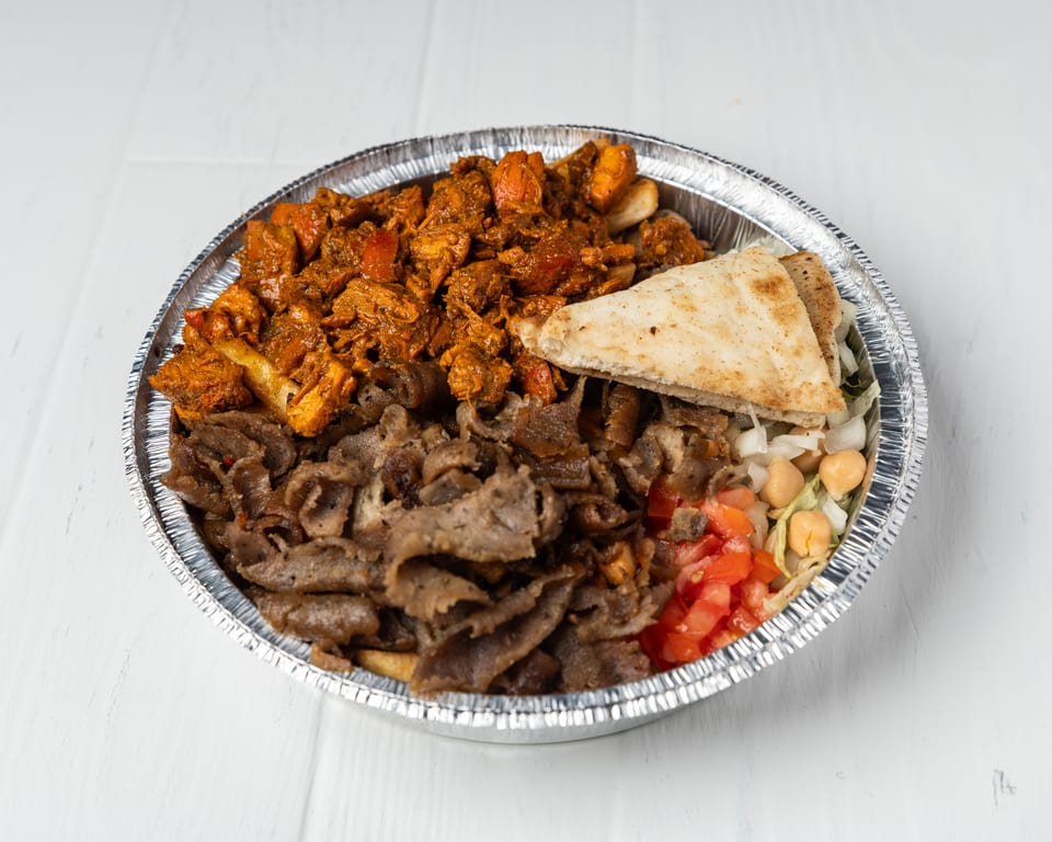 A foil container filled with chicken, gyro meat, pita bread, lettuce, chickpeas, and diced tomatoes.