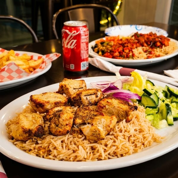Plates of chicken and rice, a burger with fries, and a soda on a dark table.