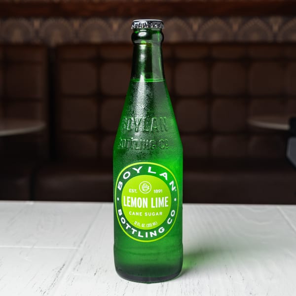 A cold, green bottle of Boylan Lemon Lime soda with condensation, on a white table.