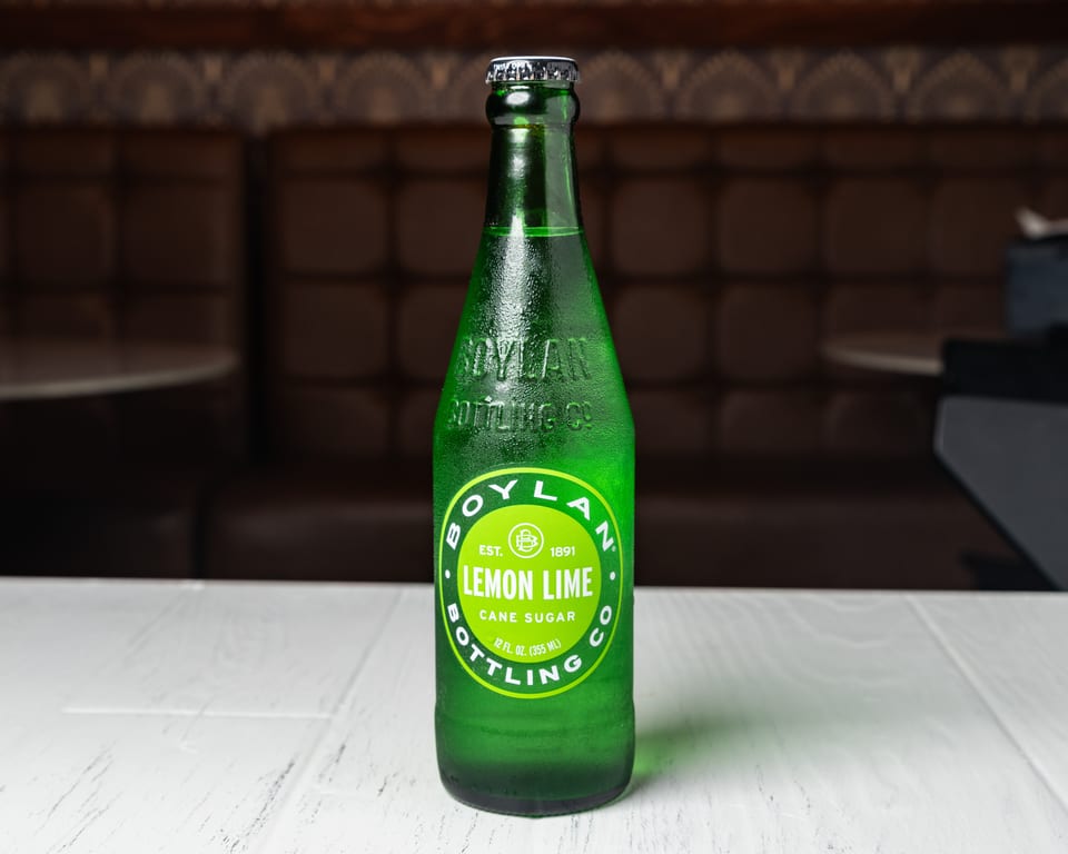 A cold, green bottle of Boylan Lemon Lime soda with condensation, on a white table.